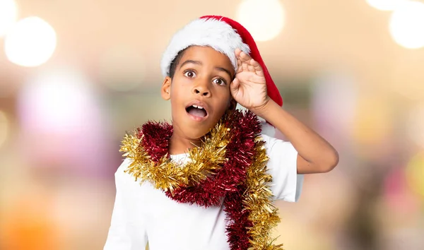戴着圣诞礼帽的非裔美国男孩 背景模糊 脸上带着惊讶和震惊的表情 — 图库照片