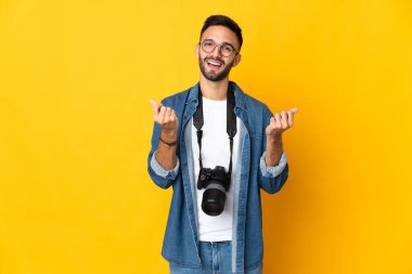 Sarı arka planda izole edilmiş genç fotoğrafçı kız para hareketi yapıyor.