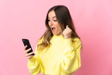 Genç Romen kadın pembe arka planda cep telefonu kullanarak ve zafer jesti yaparak izole edildi