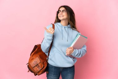 Pembe arka planda izole edilmiş genç bayan bir ürünü sunmak için kenarı işaret ediyor.