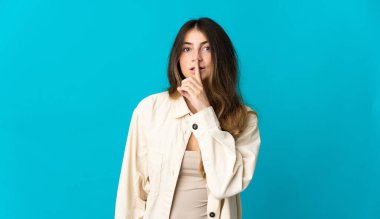 Mavi arka planda izole edilmiş beyaz bir kadın sessiz bir jest işareti gösteriyor. Parmağını ağzına sokuyor.