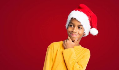 Kırmızı arka planda, Noel şapkalı Afro-Amerikalı çocuk.