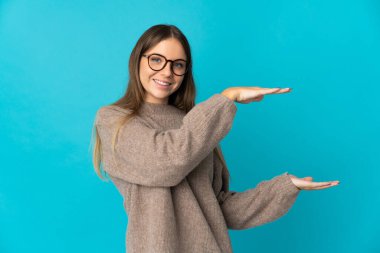 Genç Litvanyalı bir kadın mavi arka planda izole edilmiş bir ilan vermek için kopyalama alanı tutuyor