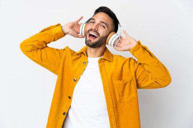 Beyaz arka planda izole edilmiş genç beyaz adam müzik dinliyor.
