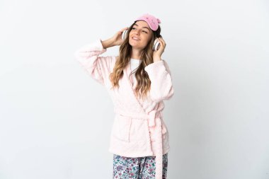 Genç Romen kadın beyaz arka planda pijamalı ve elinde yastıkla müzik dinlerken izole edildi