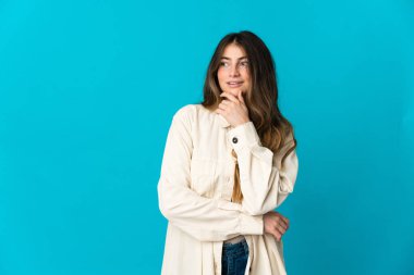 Mavi arka planda soyutlanmış genç beyaz kadın yana bakıyor ve gülümsüyor.