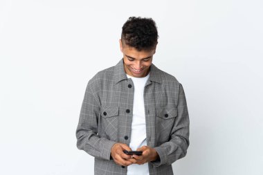 Genç Brezilyalı bir adam beyaz arka planda izole edilmiş cep telefonuyla mesaj gönderiyor.