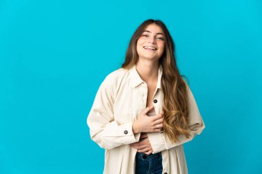 Mavi arka planda izole edilmiş genç beyaz kadın çok gülümsüyor.