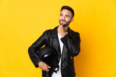 Sarı arka planda motosiklet kaskı tutan bir adam. 