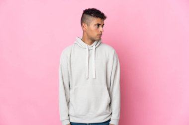 Pembe arka planda izole edilmiş genç Brezilyalı adam yan tarafa bakıyor.