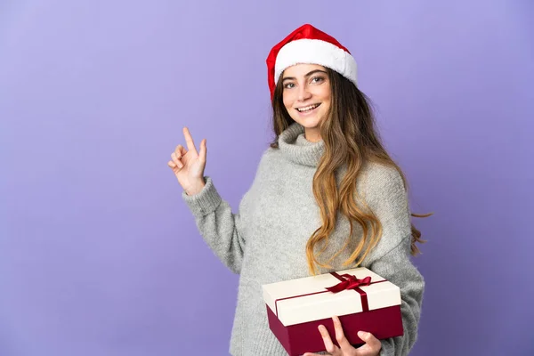 头戴圣诞礼帽的女孩 手里拿着一件白色背景的礼物 手指头指向旁边 — 图库照片