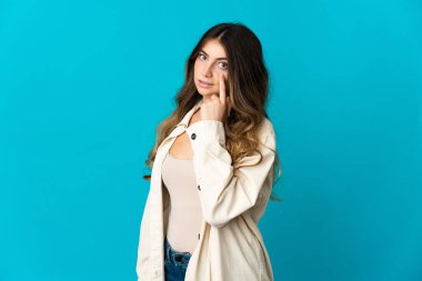 Mavi arka planda izole edilmiş genç beyaz kadın bir şey gösteriyor.