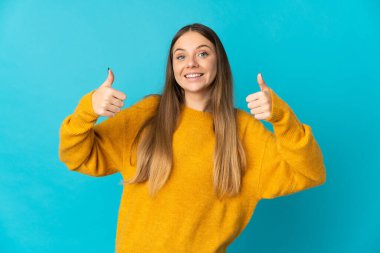 Genç Litvanyalı kadın mavi arka planda izole edilmiş bir şekilde baş parmak işareti yapıyor.