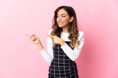 Pembe arka planda izole edilmiş genç beyaz kadın korkmuş ve kenarı işaret ediyor.