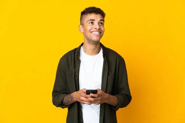 Joven Brasileño Aislado Sobre Fondo Amarillo Usando Teléfono Móvil Mirando — Foto de Stock