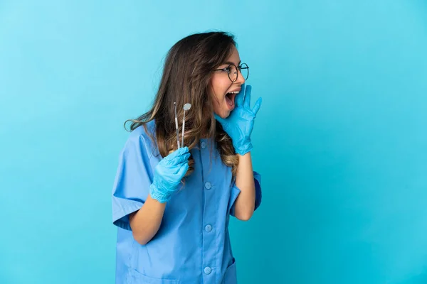 女牙医拿着工具 在蓝色背景上被隔离 大嘴巴张开 侧边喊着 — 图库照片