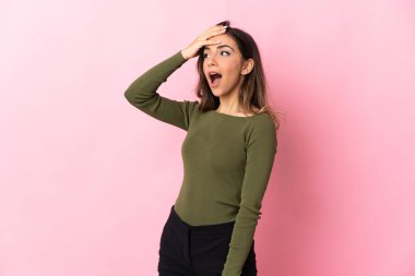 Pembe arka planda izole edilmiş genç beyaz kadın yan tarafa bakarken sürpriz jest yapıyor.