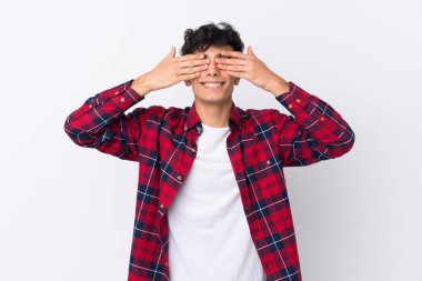 İzole edilmiş beyaz arka planda genç Arjantinli adam elleriyle gözlerini kapatıyor.