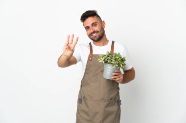 Bahçıvan beyaz arka planda bir bitki tutuyor mutlu ve parmaklarıyla üçe kadar sayıyor.