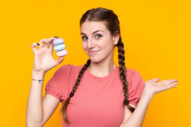 Soyutlanmış sarı arka plan üzerinde genç bir kadın renkli Fransız kurabiyeleri tutuyor ve şüpheli hareketler yapıyor.