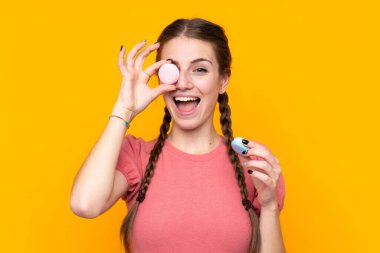 Renkli Fransız badem kurabiyeleriyle izole edilmiş sarı arka planı olan genç bir kadın.