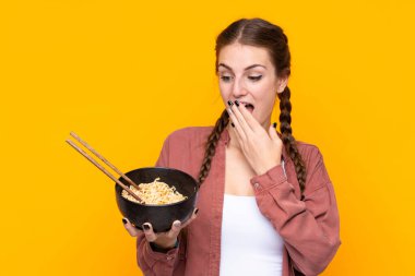 Elinde yemek çubuklarıyla bir kase şehriye tutarken şaşırmış ve şok olmuş yüz ifadesiyle izole edilmiş genç bir kadın.