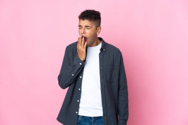 Pembe arka planda izole edilmiş genç Brezilyalı bir adam esniyor ve ağzını eliyle açık tutuyor.