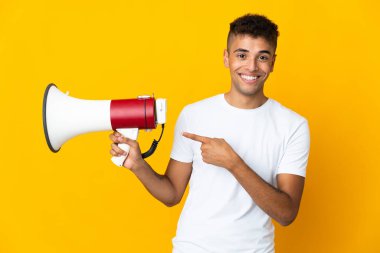 Sarı arka planda izole edilmiş genç Brezilyalı bir adam elinde megafonla işaret ediyor.