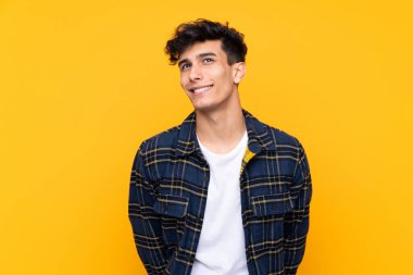 Arjantinli genç adam izole edilmiş sarı arka planda gülüyor ve yukarı bakıyor.