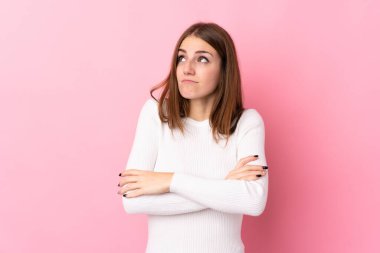 Soyutlanmış pembe arka planı olan genç bir kadın omuzlarını kaldırırken şüphe jesti yapıyor.