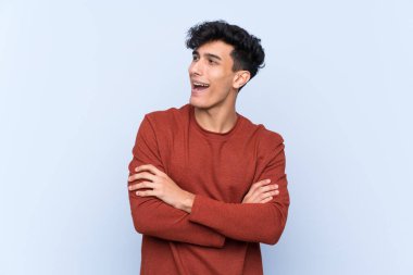 Arjantinli genç adam mavi arka planda mutlu ve gülümsüyor.