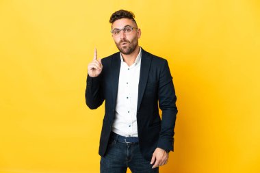 İzole edilmiş sarı arka plan üzerinde iş adamı parmağını kaldırarak çözümü anlamaya çalışıyor.