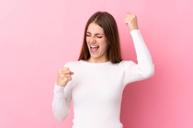 Soyutlanmış pembe arka plan zaferi kutlayan genç bir kadın.