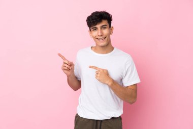 Soyutlanmış pembe arka planda genç Arjantinli bir adam işaret ediyor.