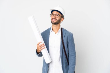 Miğferli ve elinde planları olan genç bir mimar beyaz arka planda izole edilmiş bir şekilde yukarı bakarken bir fikir düşünüyor.