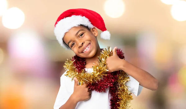 アフリカ系アメリカ人の男の子とクリスマスの帽子とともに親指アップので何か良いことが起こっているぼやけた背景 — ストック写真