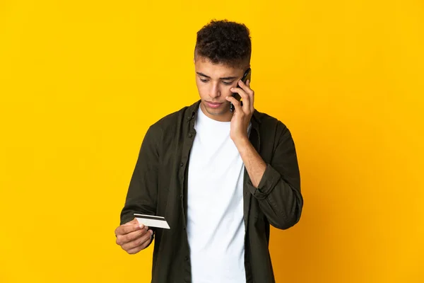 Młody Brazylijczyk Odizolowany Żółtym Tle Kupuje Komórką Kartą Kredytową — Zdjęcie stockowe
