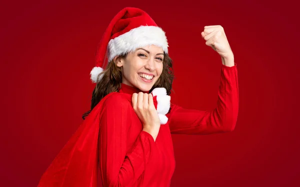 Девушка Рождественской Шляпе Держит Рождественскую Сумку Полную Подарков Изолированном Красном — стоковое фото