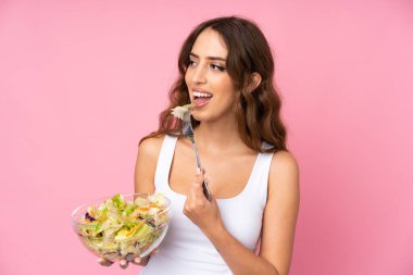 Soyutlanmış pembe duvarda salatalı genç bir kadın.