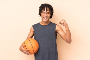 Genç Afrikalı Amerikalı adam bej arka planda izole edilmiş basketbol oynuyor ve kendisiyle gurur duyuyor.