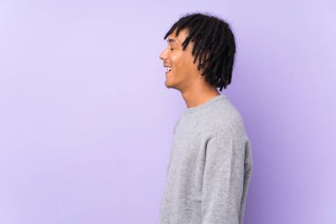 Genç Afro-Amerikalı adam mor arka planda izole edilmiş. Yan pozisyonda gülüyor.