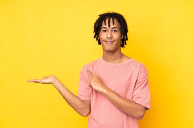 Sarı arka planda izole edilmiş genç Afro-Amerikan bir ilan vermek için fotokopi makinesini avucunun içinde tutuyor.