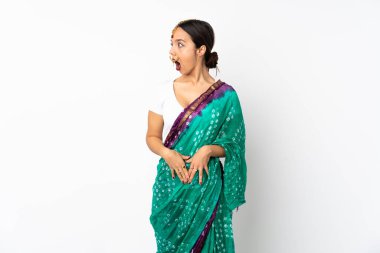 Beyaz arka planda izole edilmiş genç Hintli kadın yan tarafa bakarken sürpriz jest yapıyor.