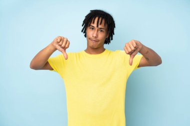 Genç Afro-Amerikan adam mavi arka planda izole edilmiş, baş parmağını aşağı gösteriyor.