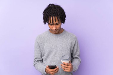 Mor arka planda izole edilmiş genç Afro-Amerikan bir adam elinde kahve ve bir cep telefonu tutuyordu.