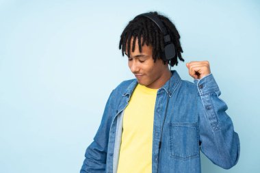 Genç Afrikalı Amerikalı adam mavi arka planda izole edilmiş müzik ve dans dinliyor.