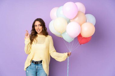 Mor arka planda izole edilmiş balonları yakalayan genç bir kadın.