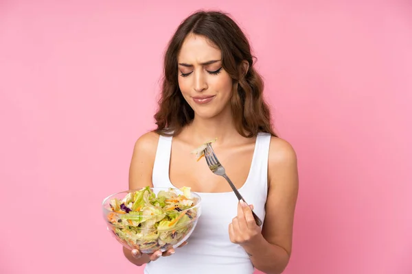 Young woman with salad over isolated pink wall