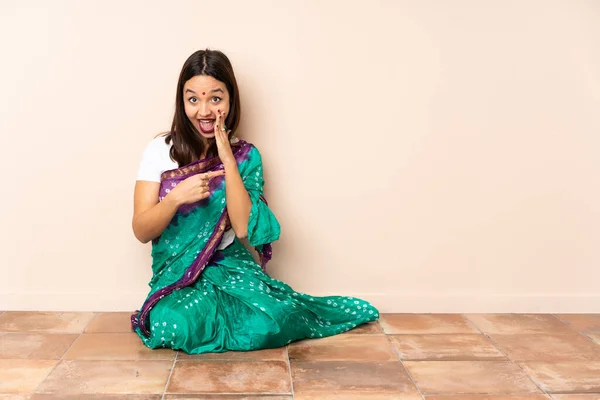 年轻的印度女人坐在地板上 指着旁边介绍产品 低声说着什么 — 图库照片
