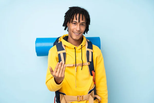 若い登山家アフリカ系アメリカ人男性と大きなバックパックを青い背景に孤立して来て招待 — ストック写真